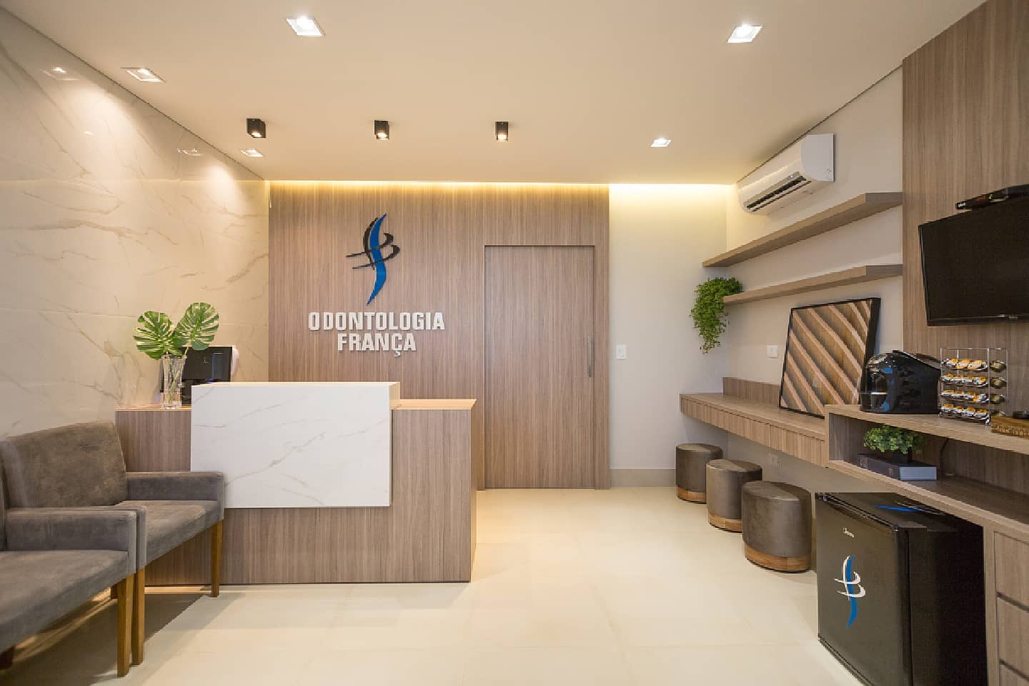 Recepção da Odontologia França com painel amadeirado, balcão de mármore, poltronas e o logotipo da clínica na parede